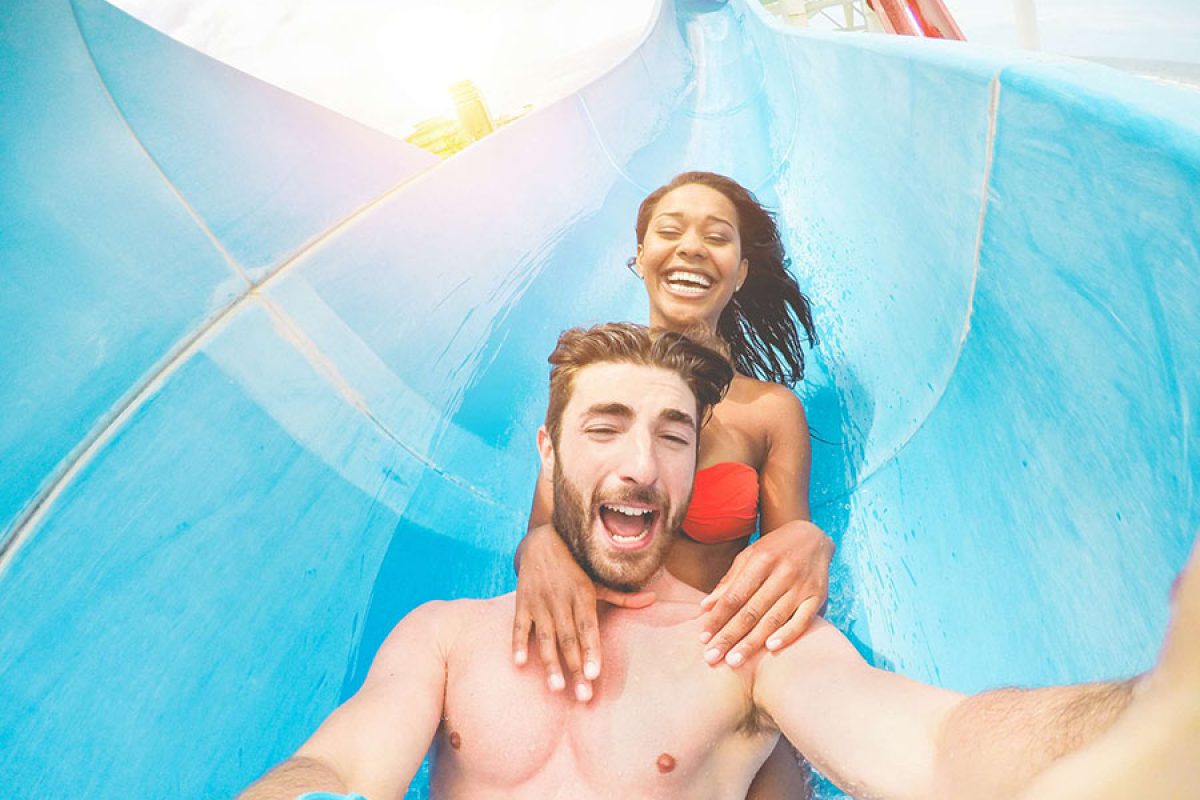 Young happy friends having fun in aqua park pipe during weekend holidays - Crazy multi race couple taking selfie photo with funny faces - Summer vacation, travel and love concept